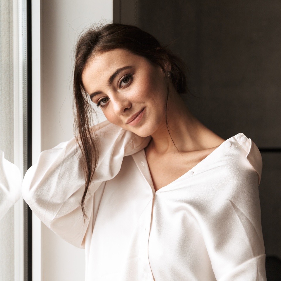 Image of gorgeous woman 30s smiling and standing near big window in living room