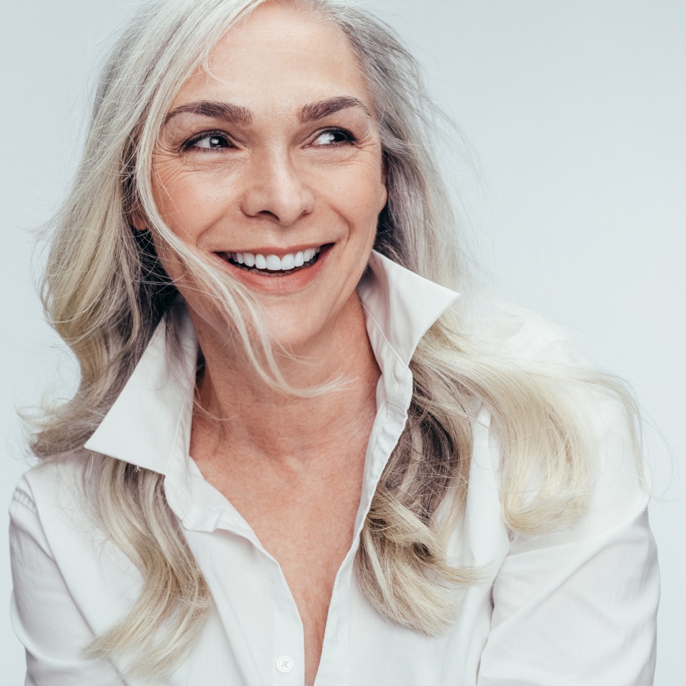 Elegant mid adult woman against white background. Stylish mature woman in white casuals looking away and smiling.