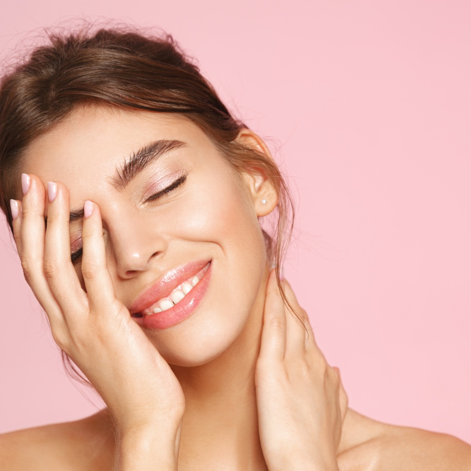 Beauty and women concept. Smiling girl with nude makeup and white teeth standing naked on pink background. Young woman touching clean healthy skin, enjoying deep hydration and moisturizing effect.