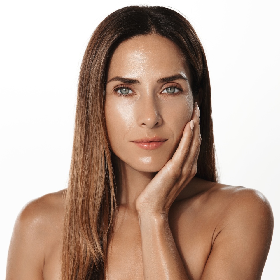 Mature skin care. Beautiful adult woman with wrinkles over eyes, touching clear, smooth nourished aging skin, fresh glow after cosmetic product, white background