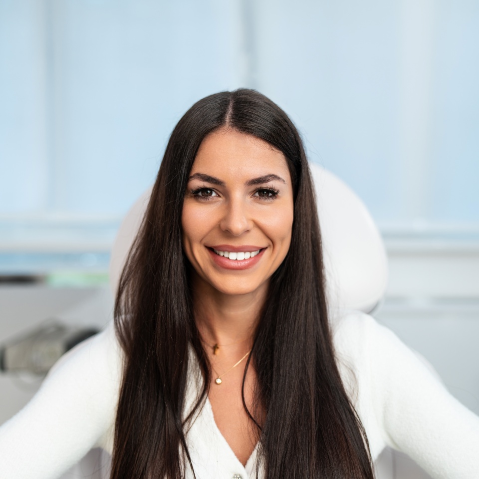 Beautiful and happy young woman sitting in medical chair and looking at camera. She is satisfied after successful beauty treatment with hyaluronic acid fillers or botulinum toxin injections.
