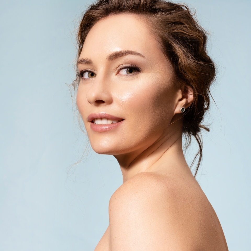Pretty female with healthy glowing moisturized skin, bare shoulders looking at camera. Studio portrait of woman pleased with skincare antiaging treatment procedure. Natural beauty, organic cosmetics
