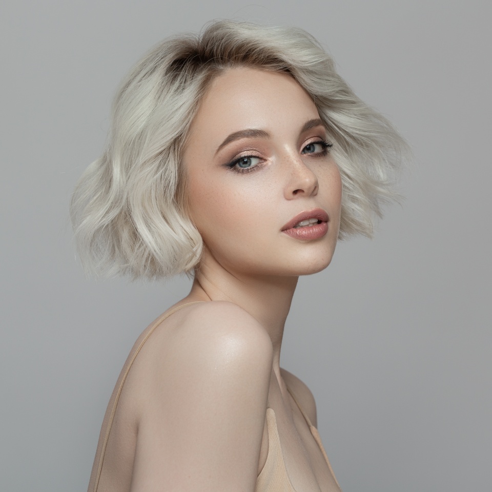 Portrait of a beautiful blonde girl with a short haircut. Gray background.