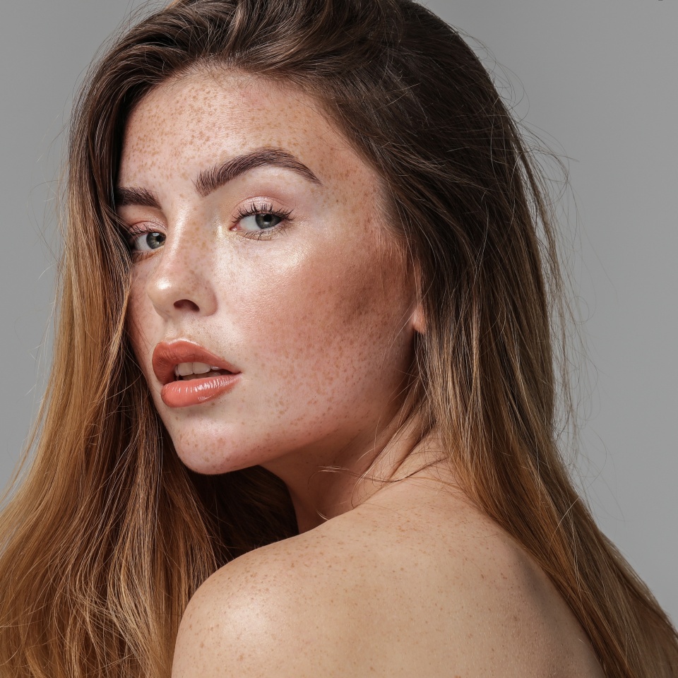 Studio beauty portrait of very natural woman with freckles on her face and shoulder. Girl looking at the camera. A lot of copy space. Skin care concept. Ideal, delicate makeup.
