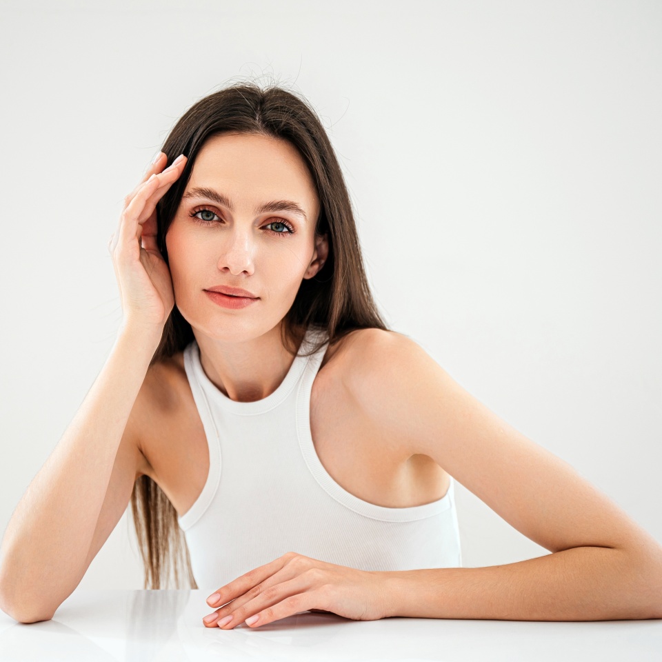 advertising of skincare and bodycare concept. studio shot of young woman with healthy radiant skin looking at camera, hold hand near face, standing isolated against copy paste grey background