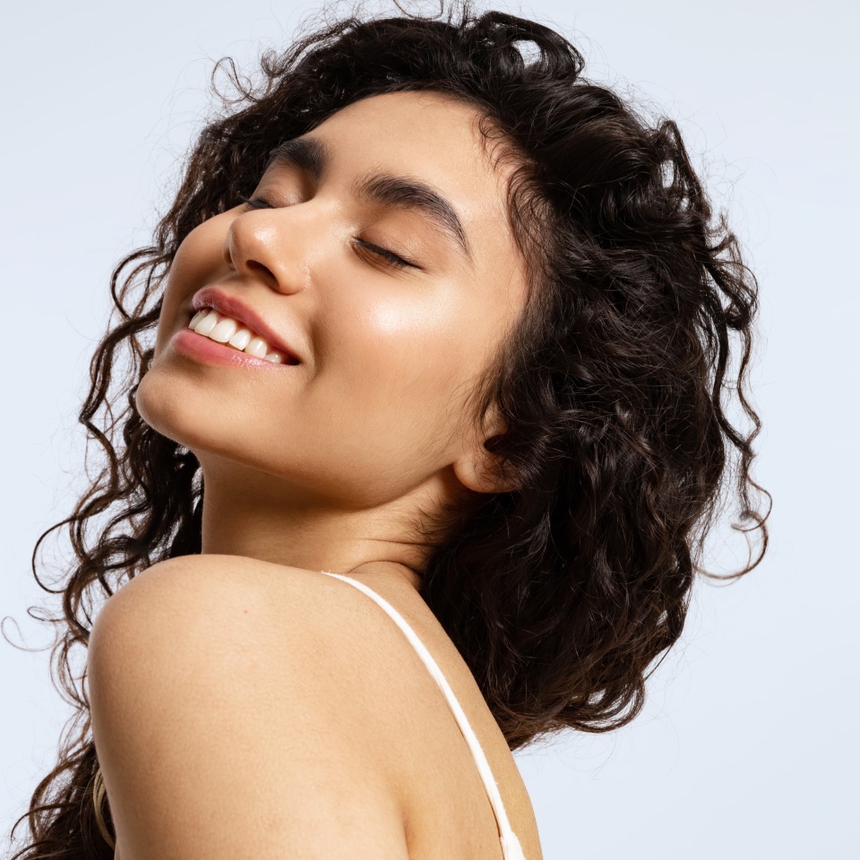 Real woman with clear skin without makeup, thick black and curly hair and glowing skin smiles