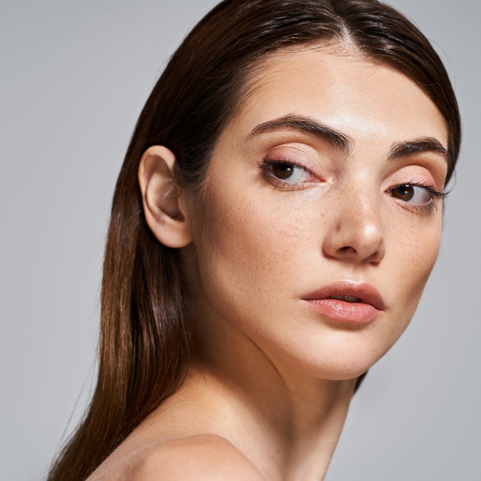 A young Caucasian woman with long brunette hair elegantly poses, exuding beauty and grace.