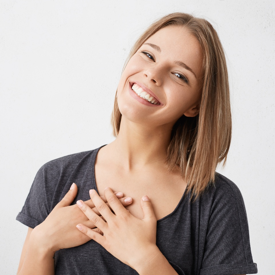 Beautiful positive friendly-looking young mixed race woman with lovely sincere smile feeling thankful and grateful, showing her heart filled with love and gratitude holding hands on her breast