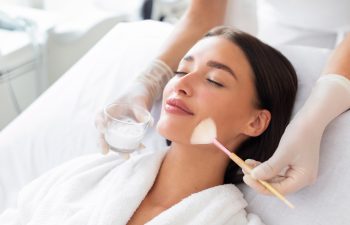 Cosmetologist cleaning face of a beautiful European woman with special gel before applying mask, peeling or scrub. Facial skin care procedures in beauty salon