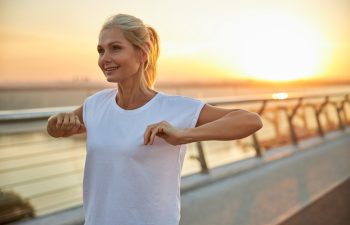 Waist-up portrait of a beautiful swarthy sporty woman in a t-shirt stretching her arms outdoors